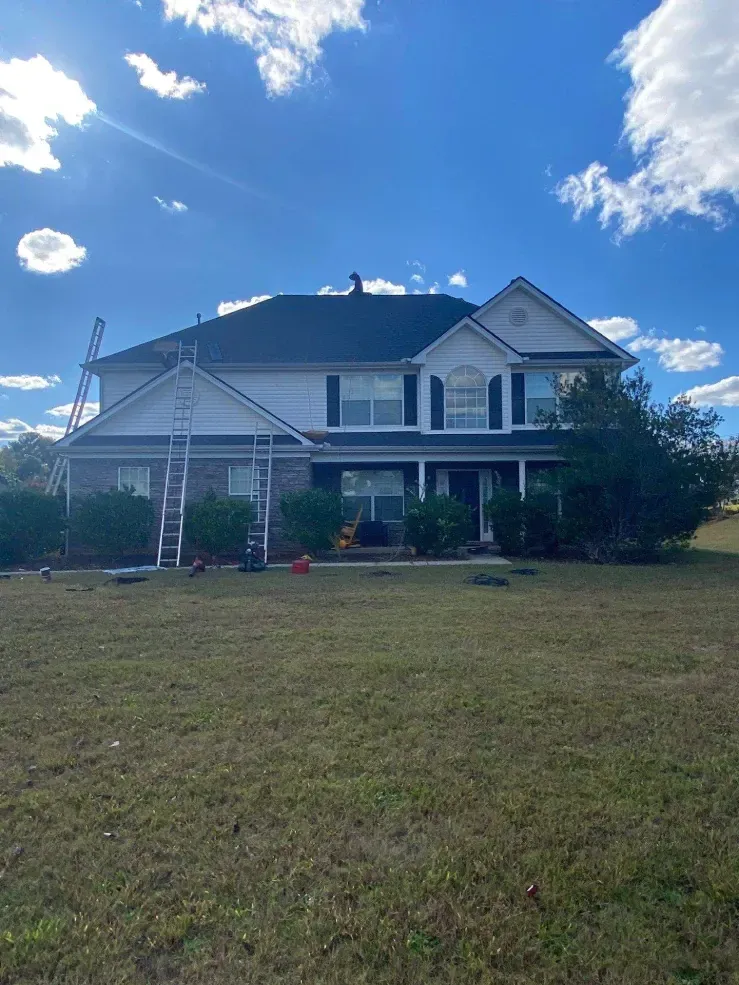 Two-story house with black roof, white trim, brick facade, and ladders leaning against the side on a sunny day.