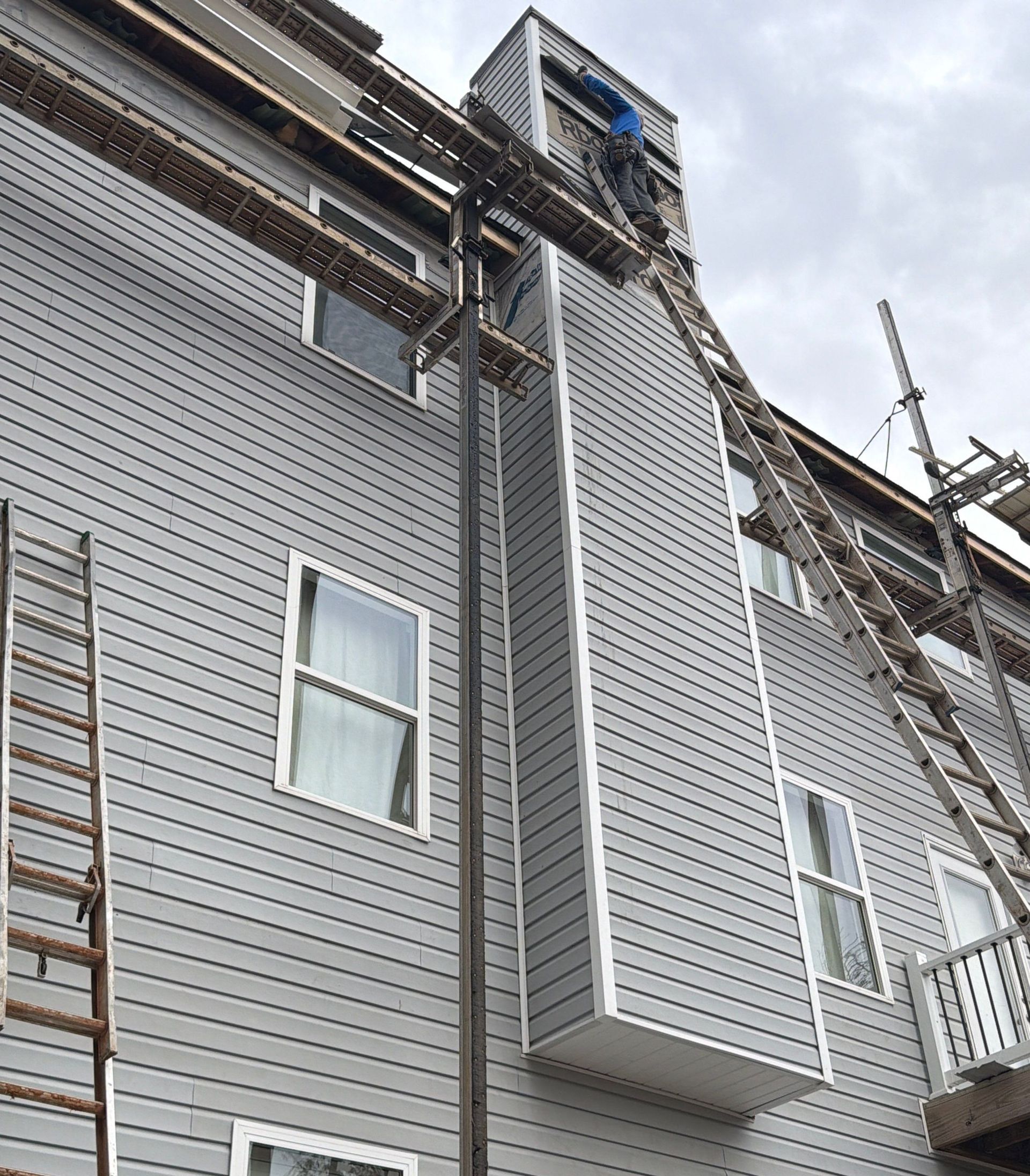 A person digs a trench in a backyard near a small excavator, a tree, and a house.