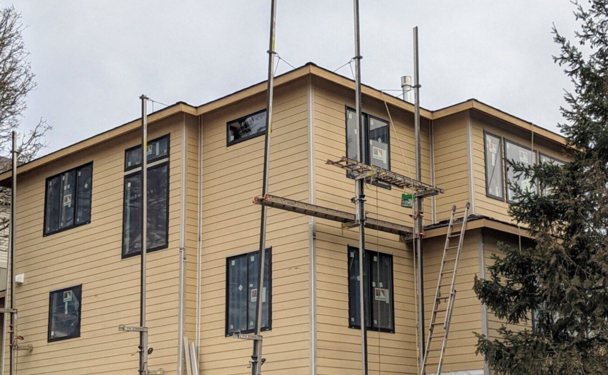 Two electricians working on an electrical panel outside a building. One holds a cable.