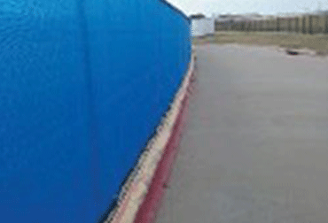 Blue-walled structure next to a concrete path, with a grassy area in the background.