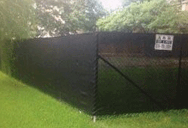 Black privacy fence in a grassy yard. Trees in the background.