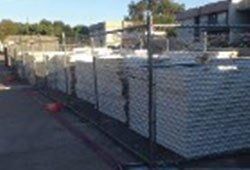 Gray cement blocks stacked behind a chain link fence. Outdoors with trees in the background.