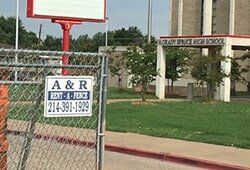 Sign on chain-link fence at Grady Spruce High School with phone number 214-391-1929.