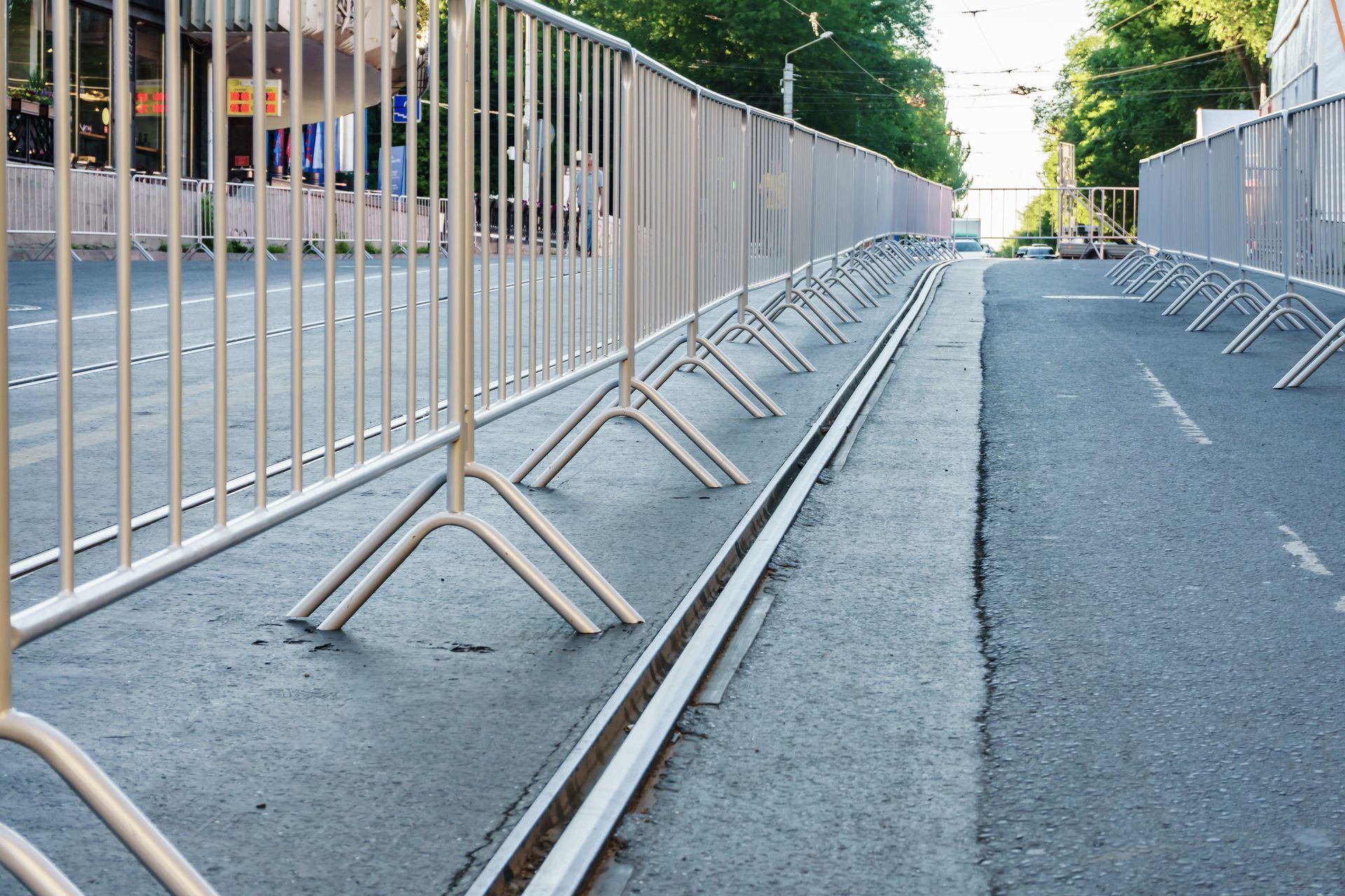 Metal control barriers lined along an empty paved street, forming a temporary pedestrian barrier.