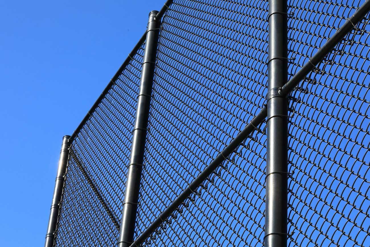 Tall chain-link temporary construction fence with steel poles against clear blue sky.
