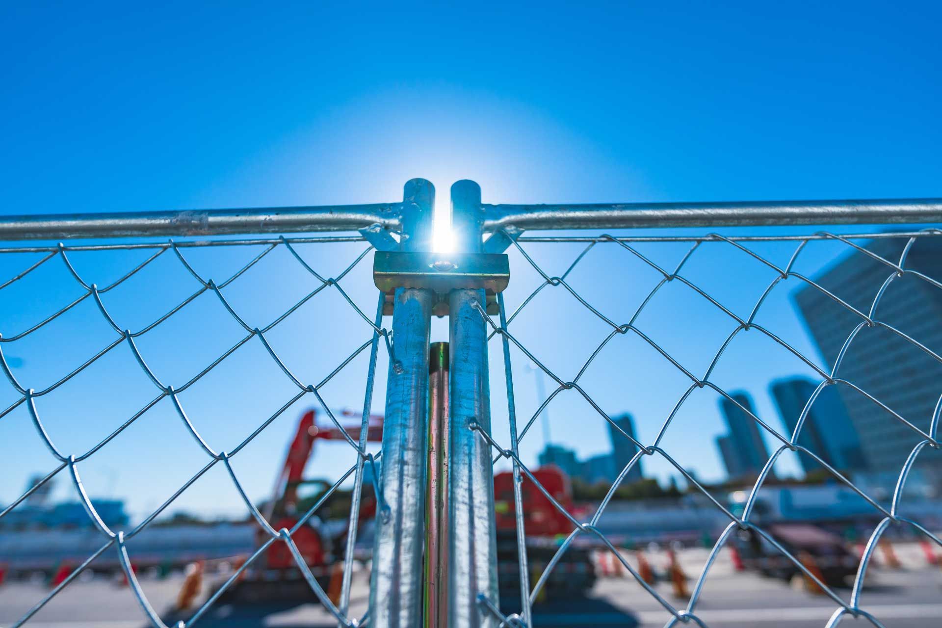 Chain-link fence blocking access to a urban construction site with sun glare. Chain-link fence blocking access to a urban construction site with sun glare.