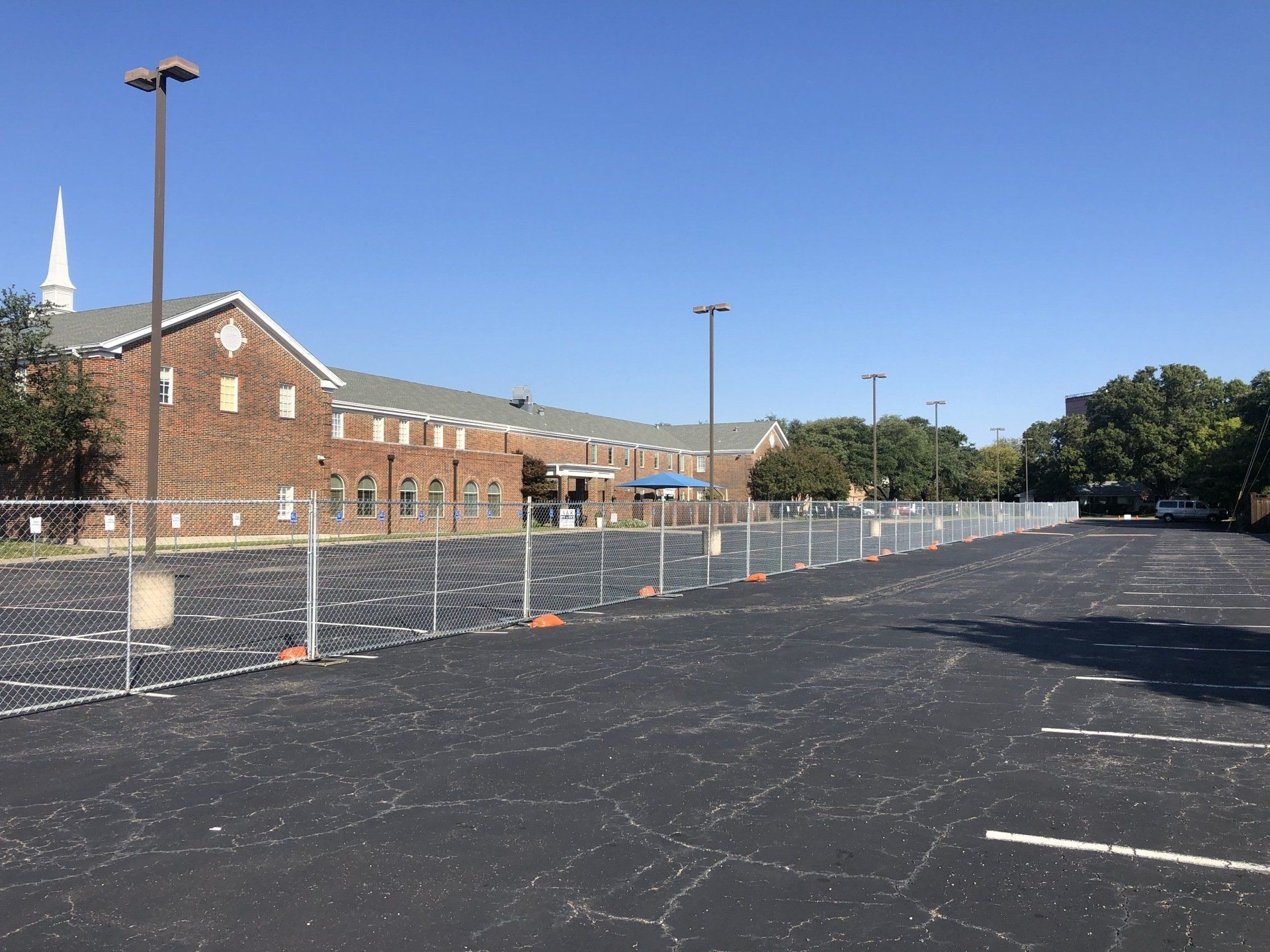 Chain link fence blocking off a parking lot in front of a brick building. Clear sky overhead.
