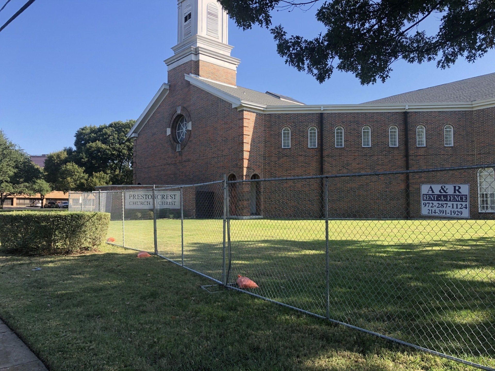 A brick church with a fenced yard and a sign for A&R. Green grass and blue sky.