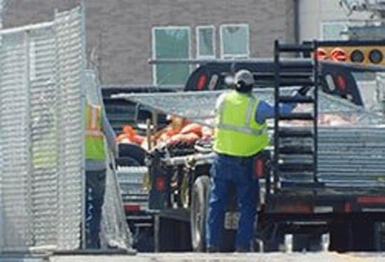 Construction workers near a truck, wearing vests, next to scaffolding.