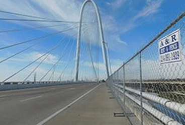 White arch bridge over road, blue sky background. A&R rent fence in foreground. Dallas, Texas.