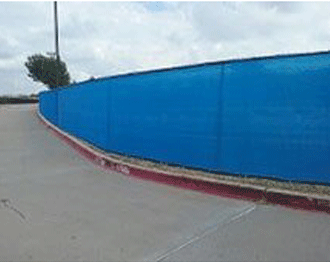 Blue privacy fence along a gray road with a red curb, under a cloudy sky.