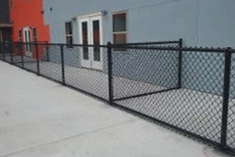 Black chain-link fence in front of a building with double doors and windows on a concrete patio.