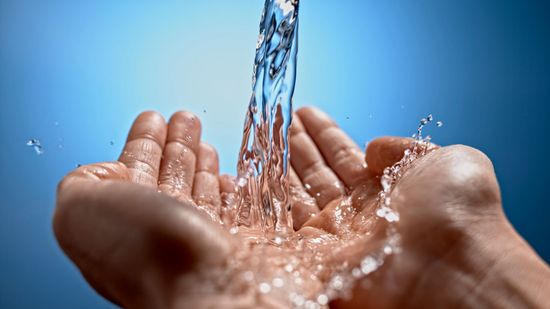 Hands cupped, catching a stream of clear water against a blue background. Hands cupped, catching a stream of clear water against a blue background.