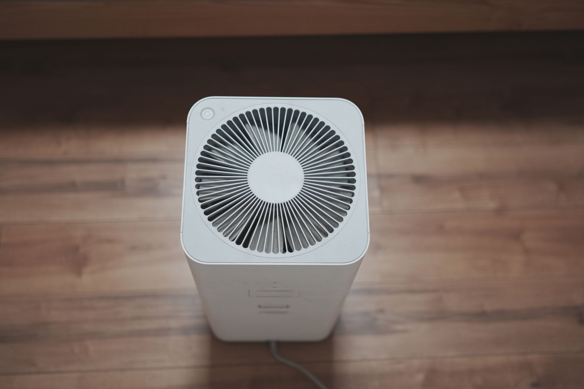 White air purifier on a wooden floor with a top vent and a power cord.