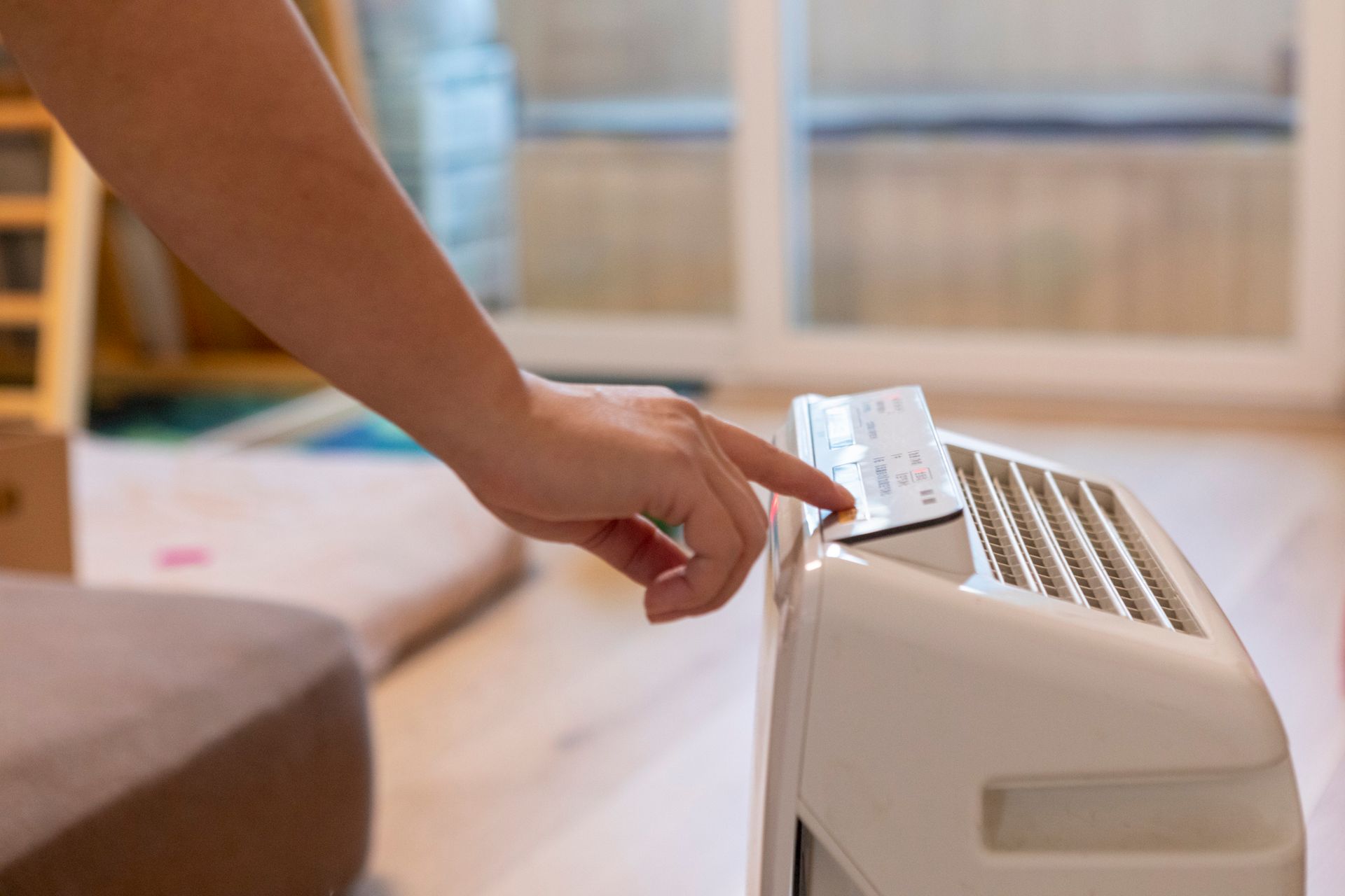 Person's hand pressing a button on a white air purifier in a room.