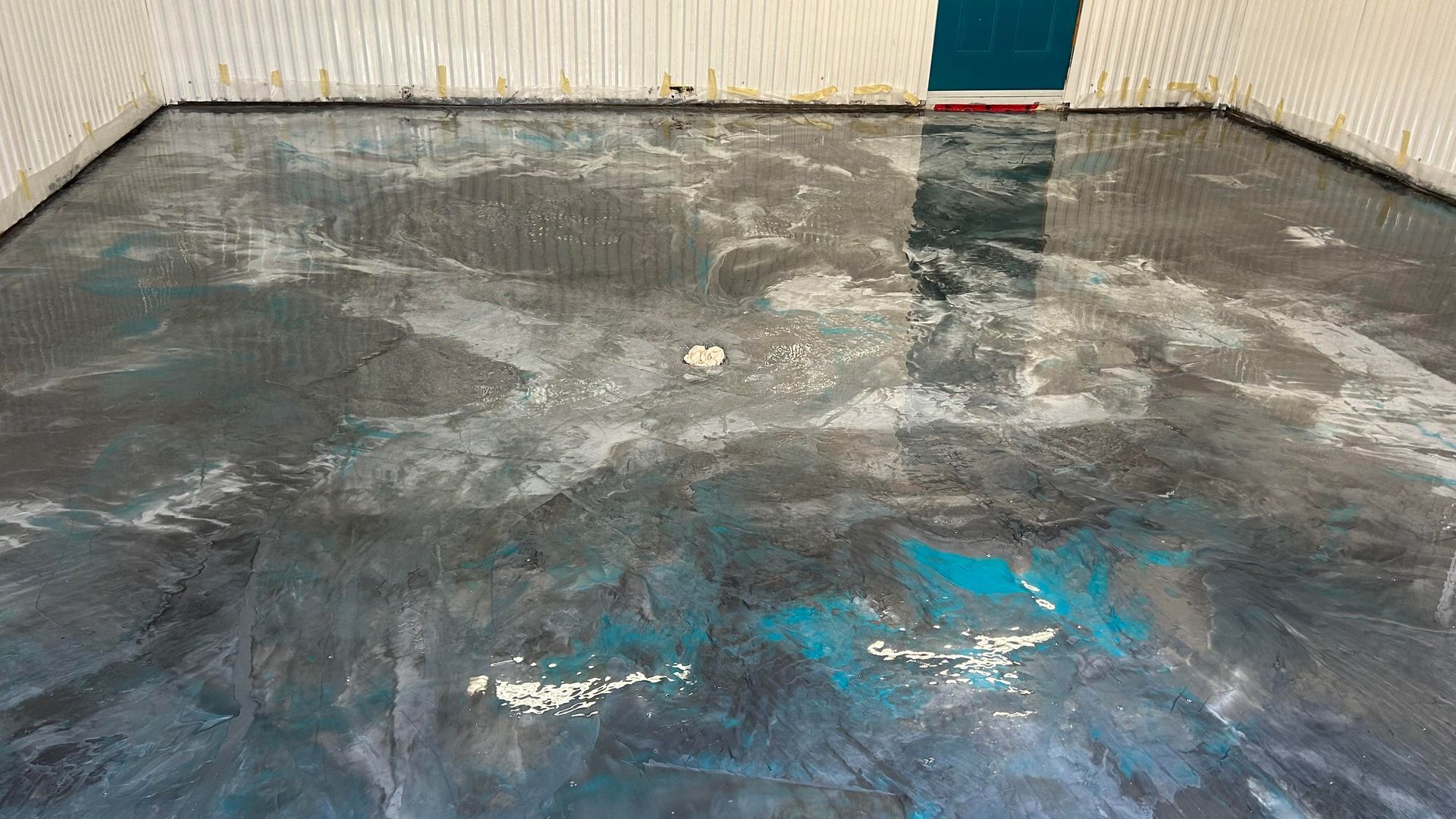 Sol époxy gris et bleu sarcelle avec des accents blancs dans une pièce, certains murs visibles.