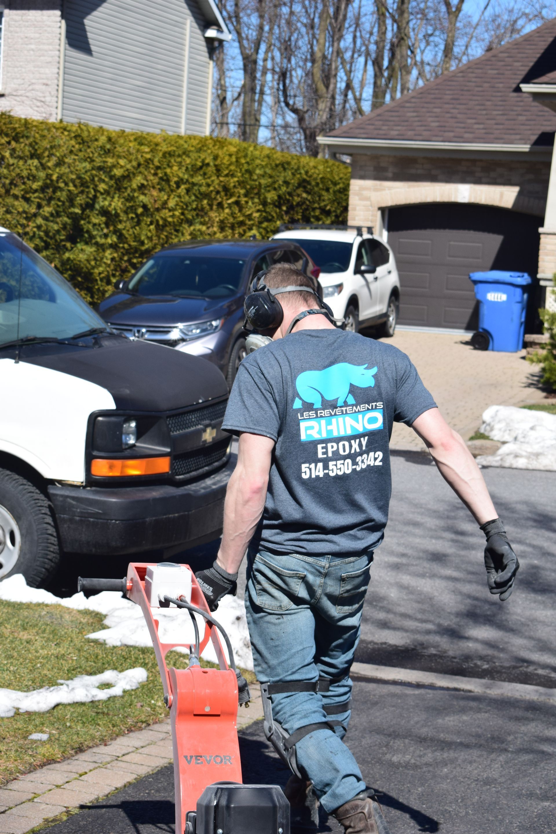 Un homme portant des écouteurs pousse une souffleuse à neige dans une allée.