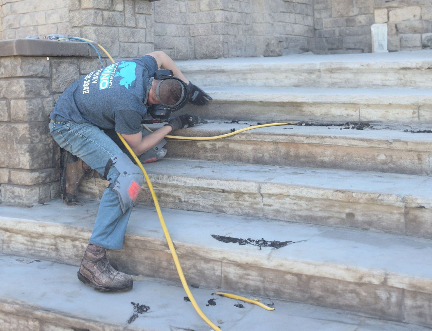 Un homme répare un escalier en béton, agenouillé, à l'aide d'un outil relié à un tuyau jaune.