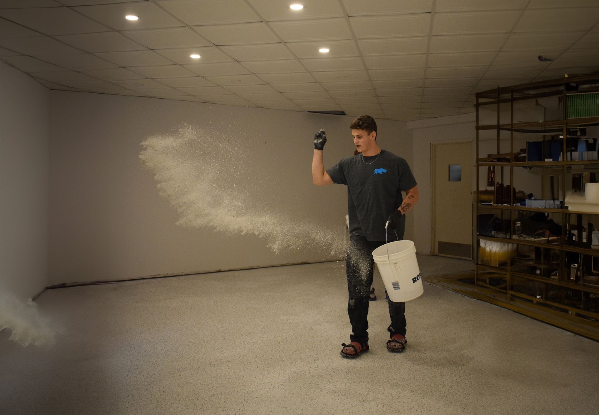 Un homme jette de la poudre blanche, probablement de la poussière, contre un mur dans une pièce vide.
