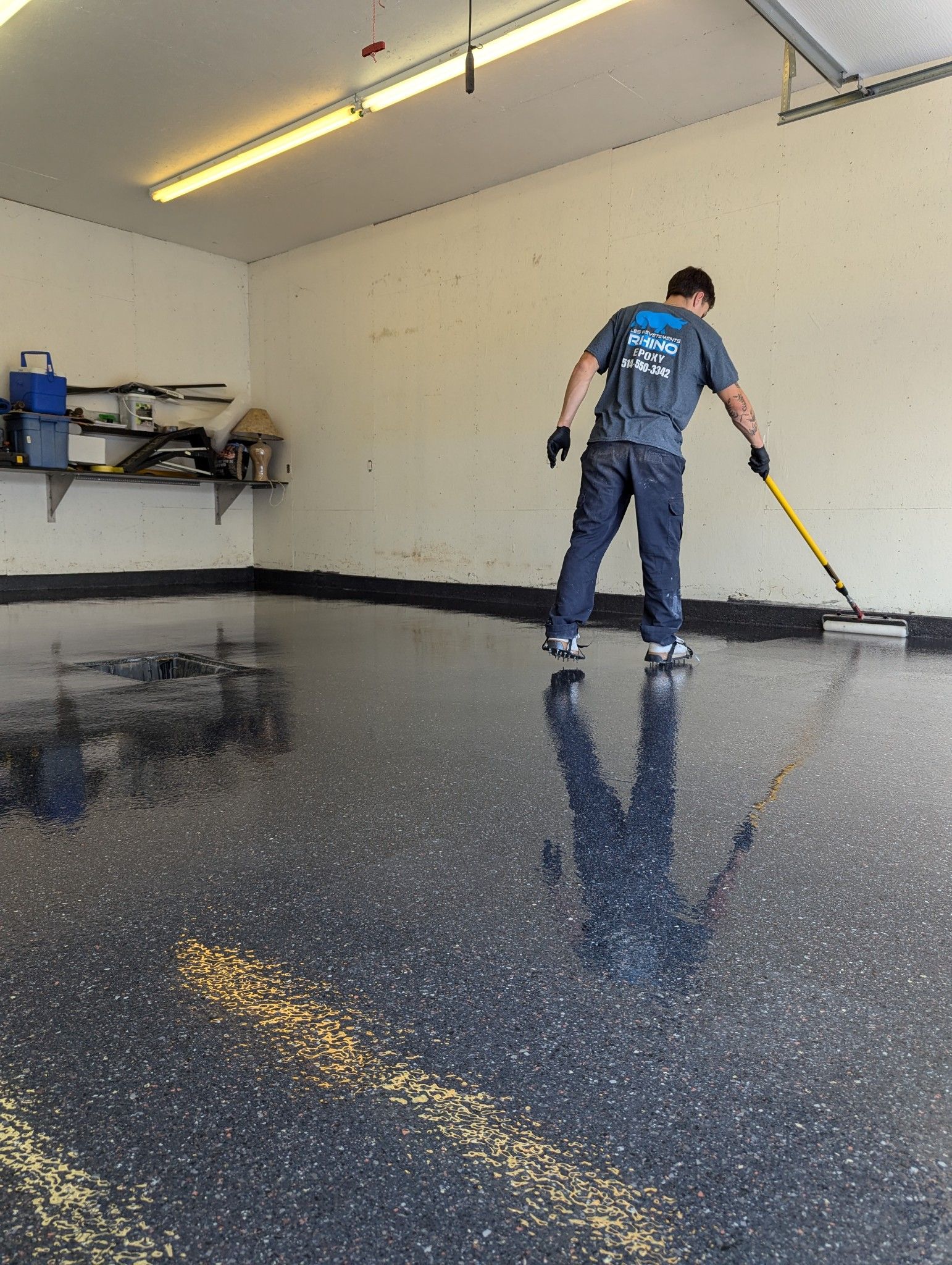 Un homme peint le sol d'un garage avec un rouleau.