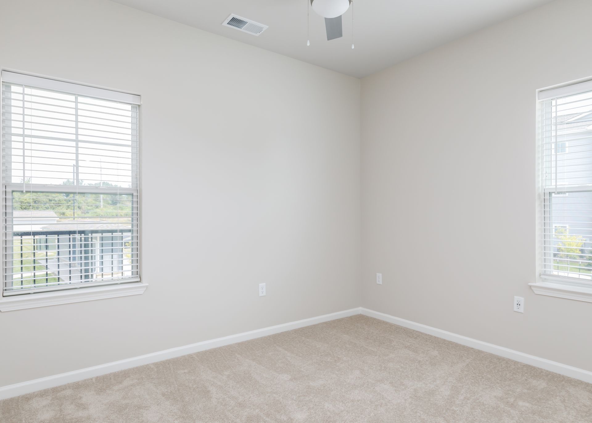 An empty bedroom with two windows and a ceiling fan.