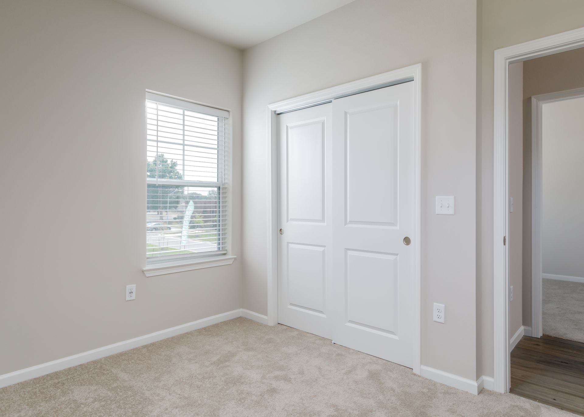 An empty bedroom with a window and a closet.
