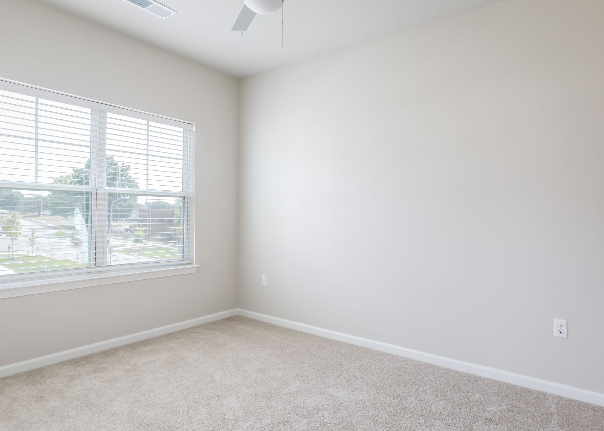 An empty bedroom with a window and a ceiling fan.