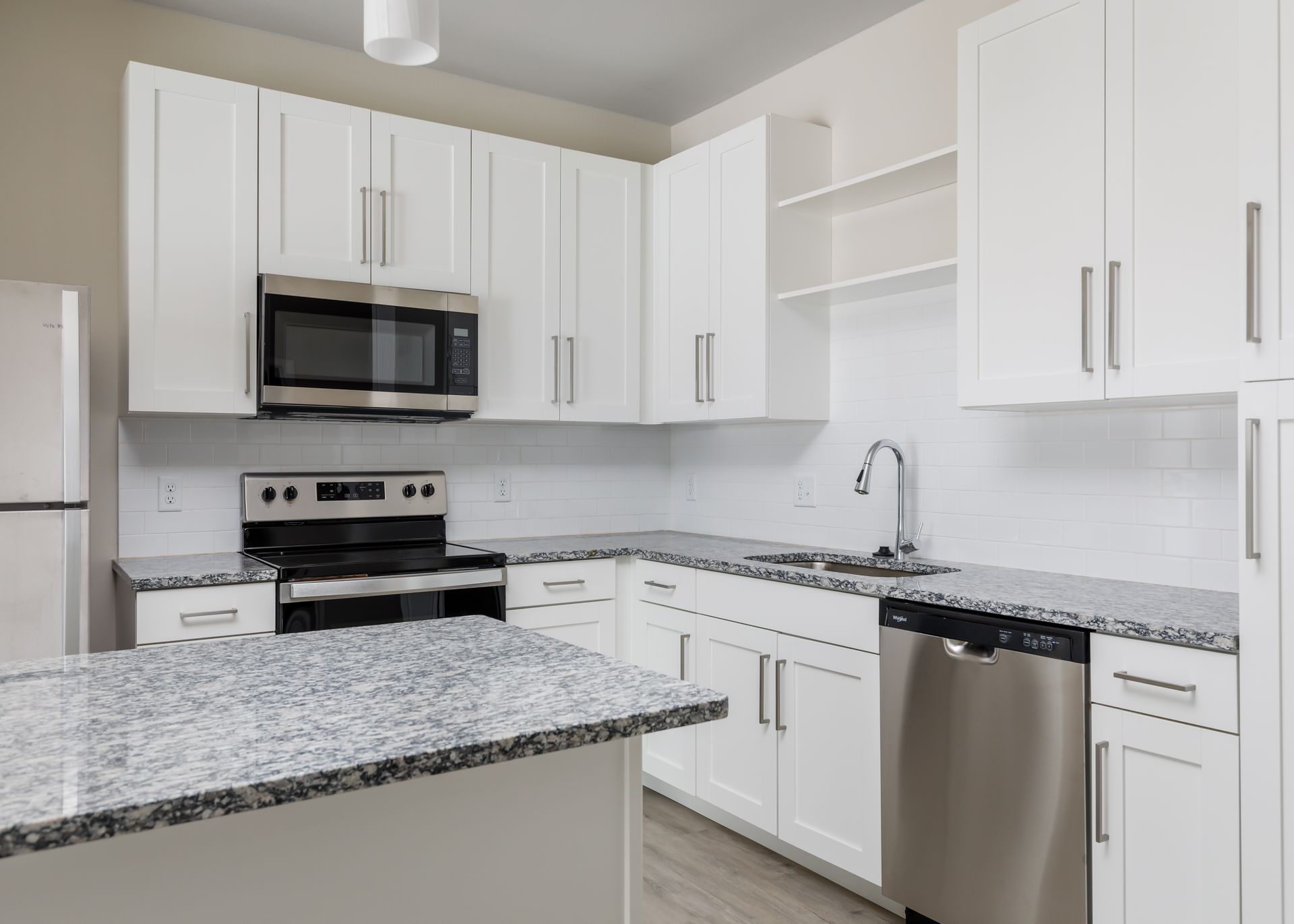 A kitchen with white cabinets , granite counter tops , stainless steel appliances and a refrigerator.