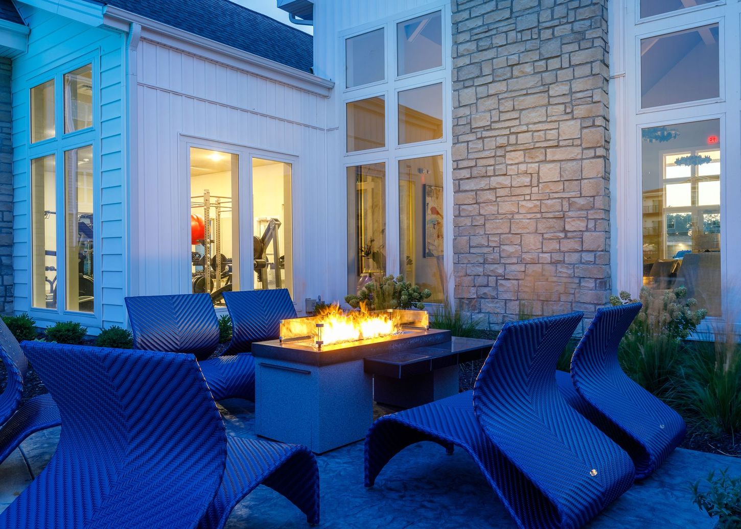 A patio with blue chairs and a fire pit in front of a building.