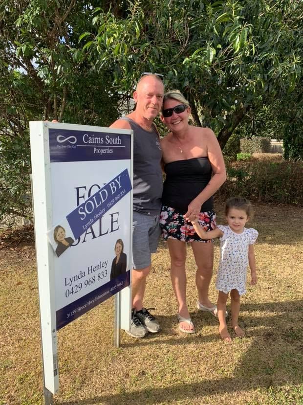 A Man, Woman And Child Are Standing In Front Of A Sold By Sale Sign — Cairns South Properties In Edmonton, QLD