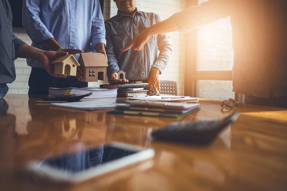 A Group of People Are Sitting Around a Table Looking at a Model House — Cairns South Properties In Edmonton, QLD