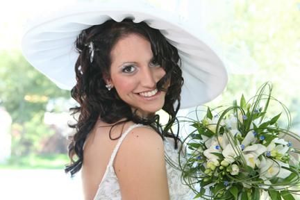 La mariée porte un chapeau blanc et tient un bouquet de fleurs.