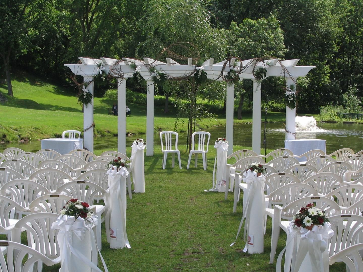 Des rangées de chaises blanches sont alignées devant une pergola blanche