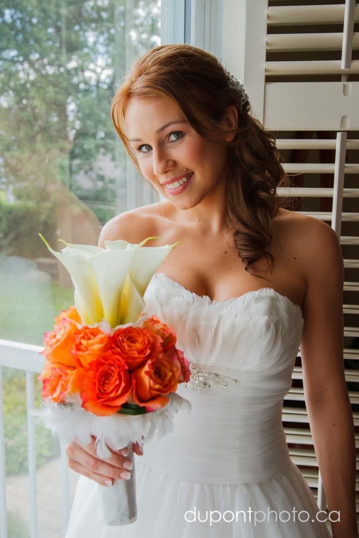 Une femme en robe blanche tient un bouquet de fleurs orange et blanches.