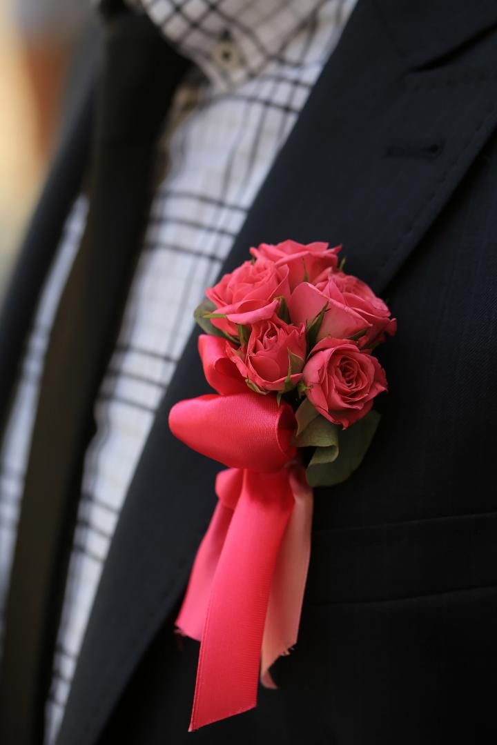 Un homme en costume a une boutonnière avec des roses roses et un ruban rose