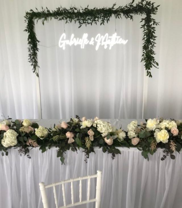 Une table avec des fleurs et une enseigne au néon sur laquelle est écrit Gabrielle et Matthew