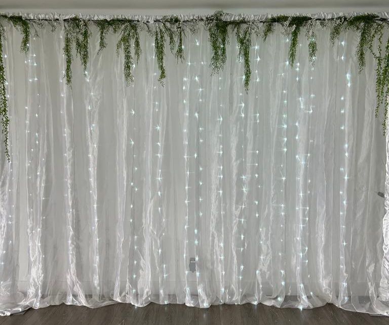 Un rideau blanc avec des lumières et de la verdure suspendues.