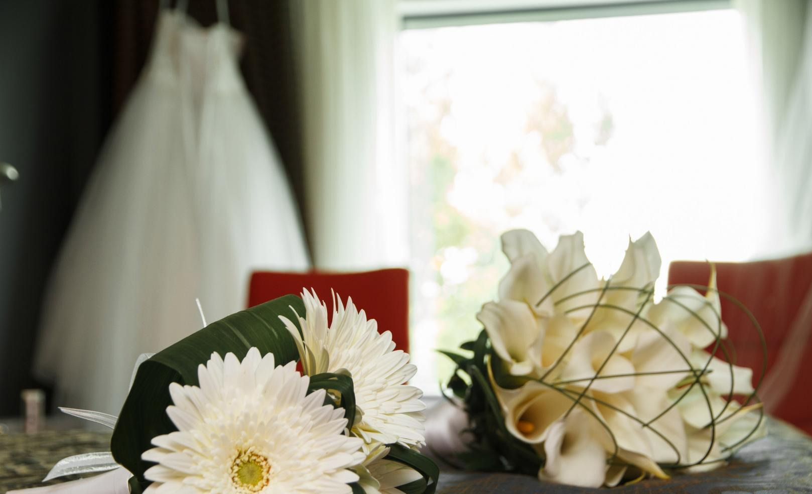Un bouquet de fleurs blanches est posé sur une table avec une robe de mariée en arrière-plan.