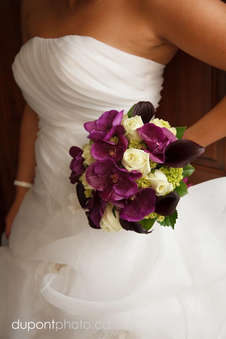 Une femme en robe blanche tient un bouquet de fleurs violettes et blanches