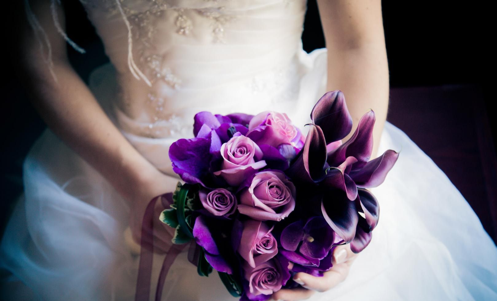 Une mariée en robe blanche tient un bouquet de fleurs violettes.