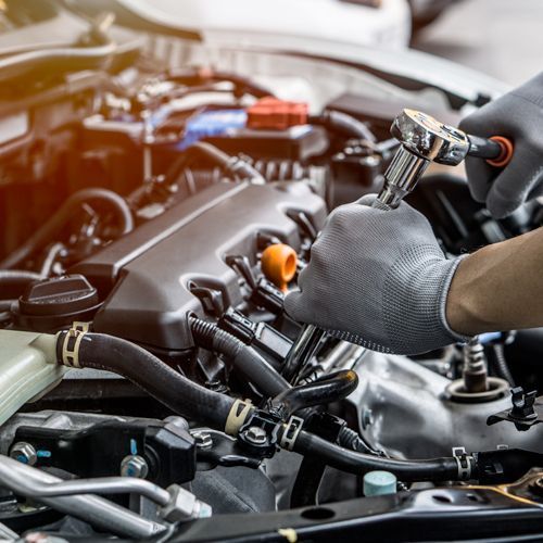 Mechanic using a wrench to work on a car engine in a garage, wearing gray gloves.