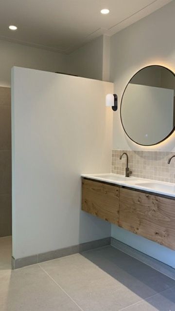 Moderne badkamer met witte muren, zwevend houten badmeubel, ronde spiegel en tegelachterwand.