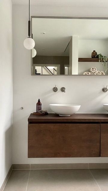 Moderne badkamer met houten badmeubel, witte waskommen, grote spiegel en hangende bolvormige lamp van Nuura