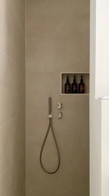 Douche met beige tegels, nis met bruine flessen, handdouche.