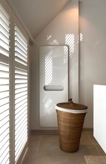 Hoek van de wasruimte: witte Shutters, moderne elektrische handdoek radiator, rieten wasmand, beige tegelvloer.