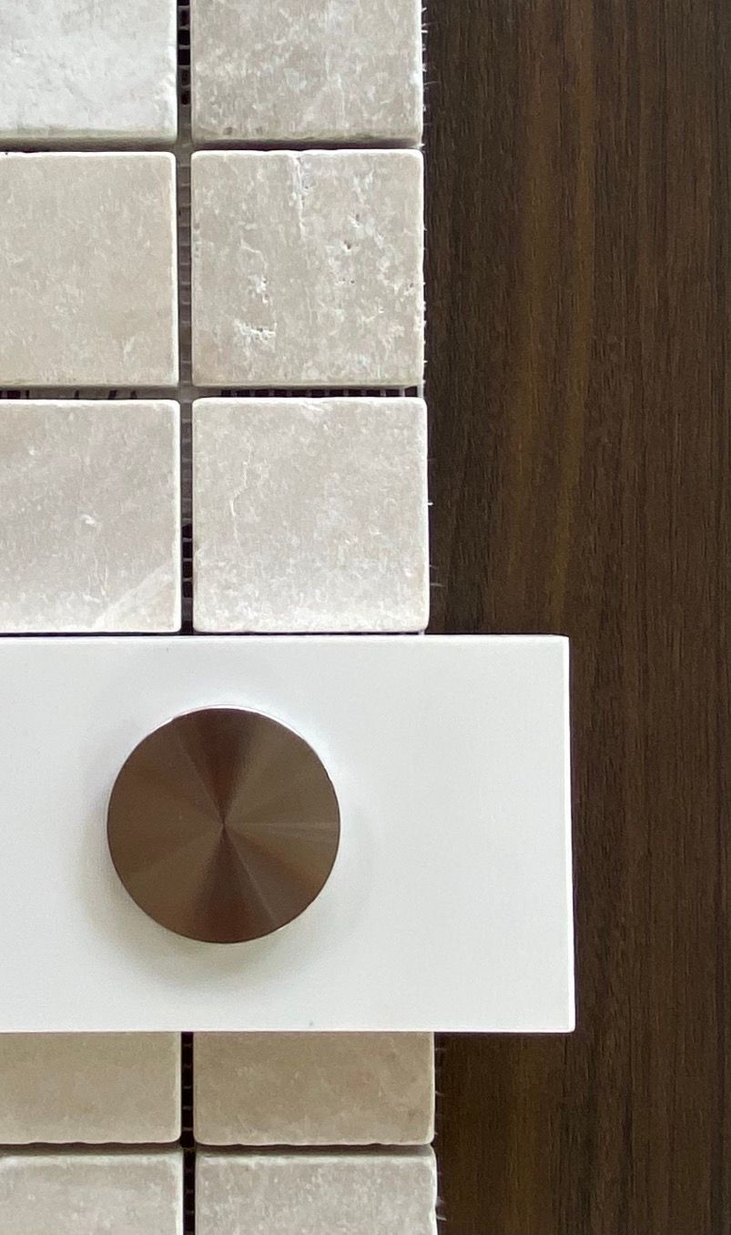 Detailopname: lichte vierkante marmeren tegels, Solid Surface met bronzen knop, naast een houten paneel.