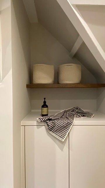 Crèmekleurige opbergnis met twee manden op een houten plank. Op het kastje eronder staan ​​een fles en een geruite handdoek.