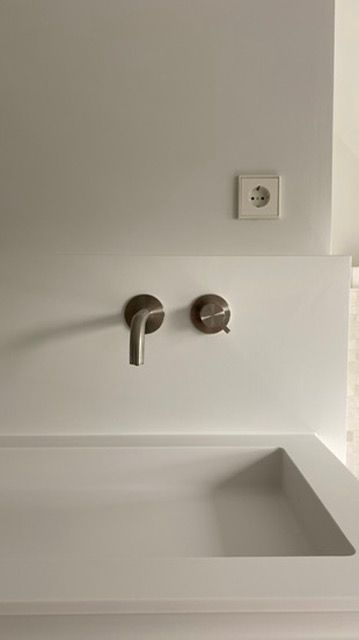 Witte Solid Surface wastafel met zilverkleurige  RVS kraan en knop tegen een witte muur. 