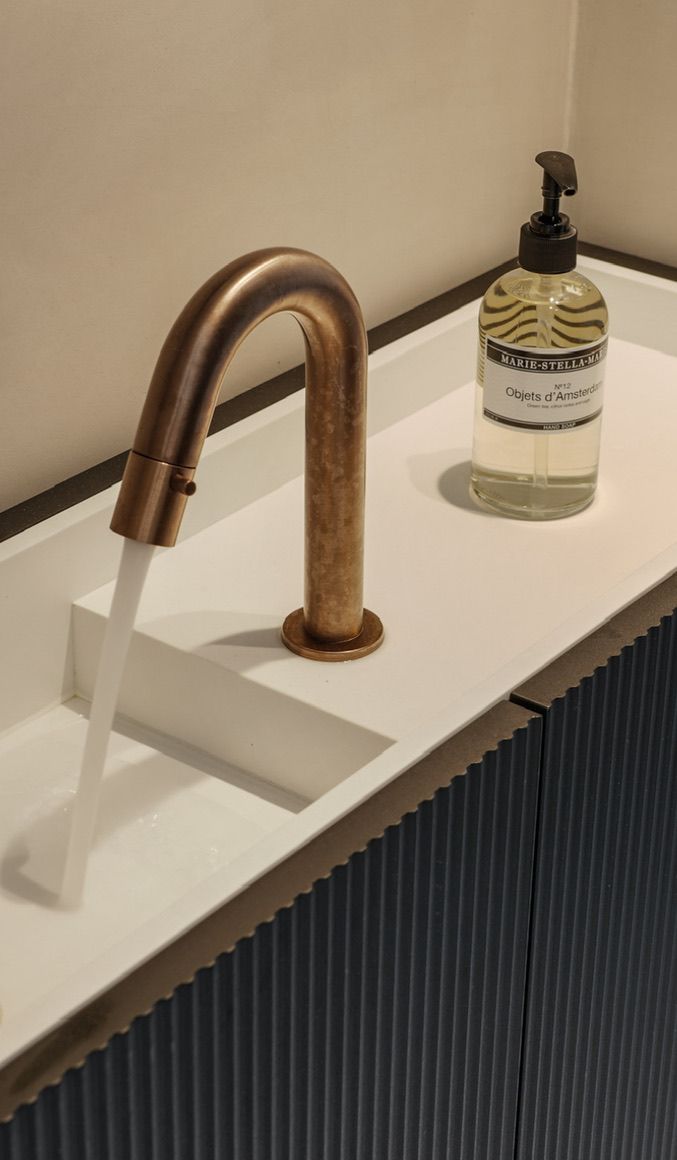 Koperen kraan die water in een Solid surface  wasbak laat stromen, zeepfles op het aanrecht, zwart fontein kastje.