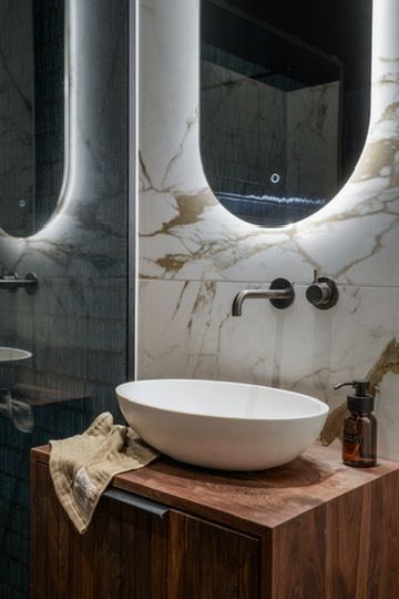 Badkamermeubel met marmeren achterwand, ovale spiegel met achtergrondverlichting, opbouwspoelbak en houten walnoot kast.